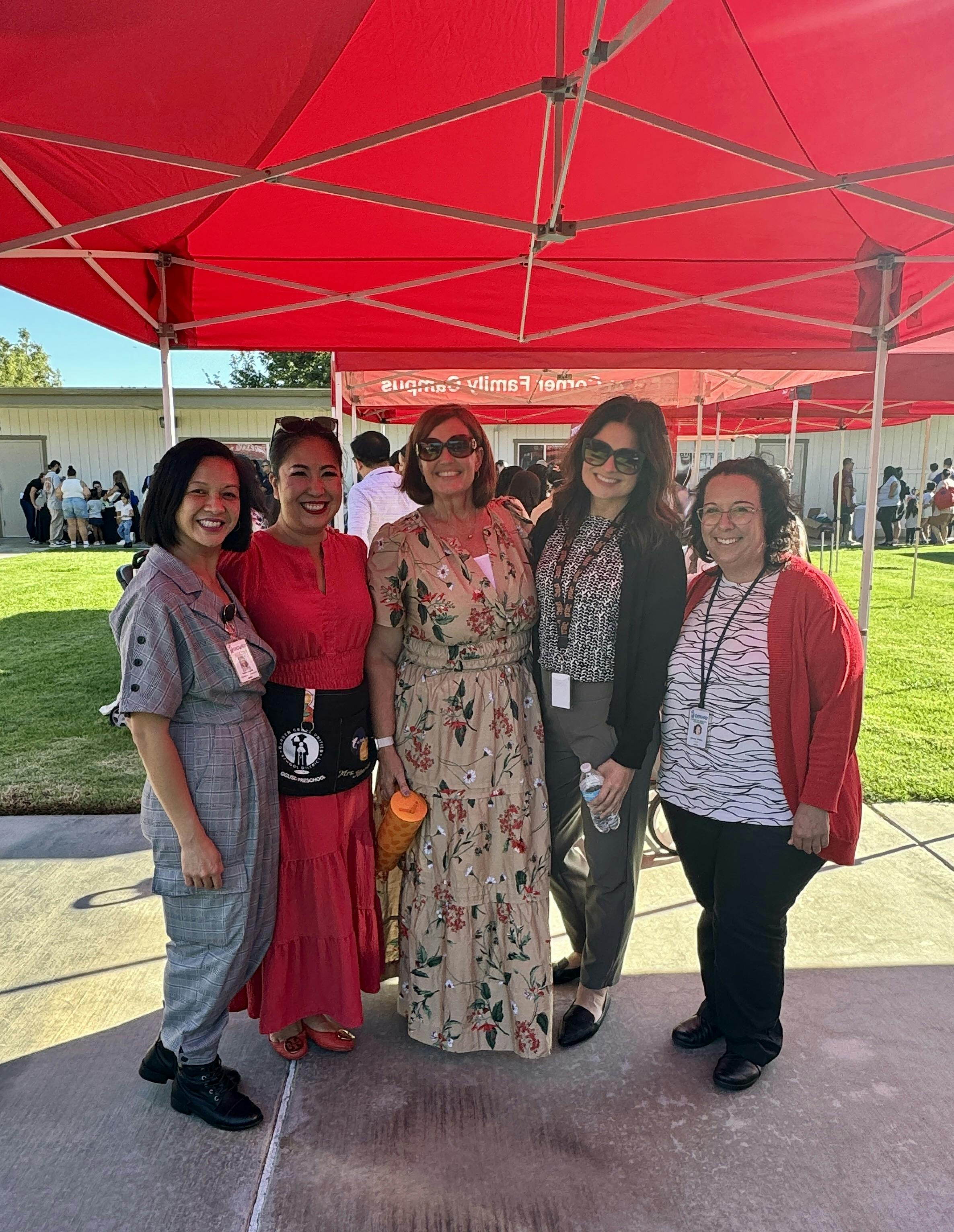 Five people standing together under a red canopy outdoors