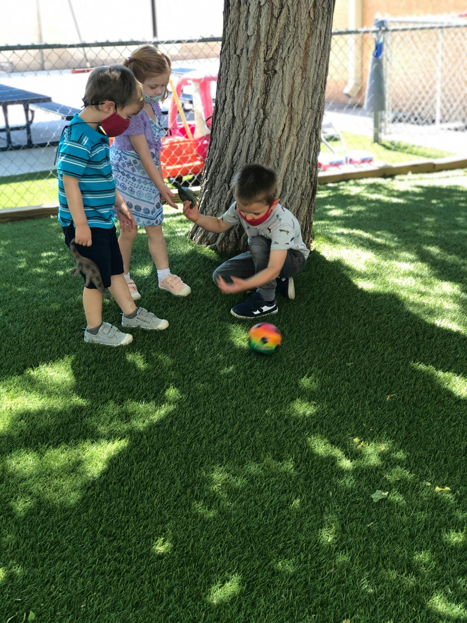 Three children playing with a ball on grass near a tree