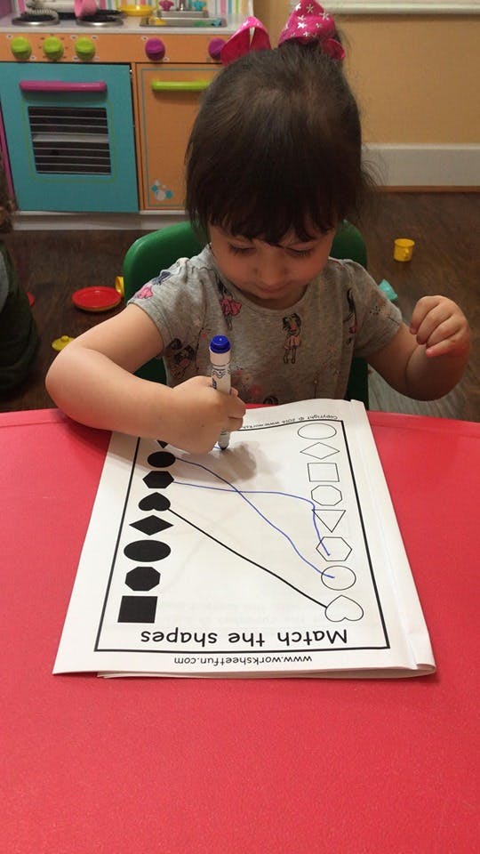 Child drawing on a worksheet with a marker, matching shapes