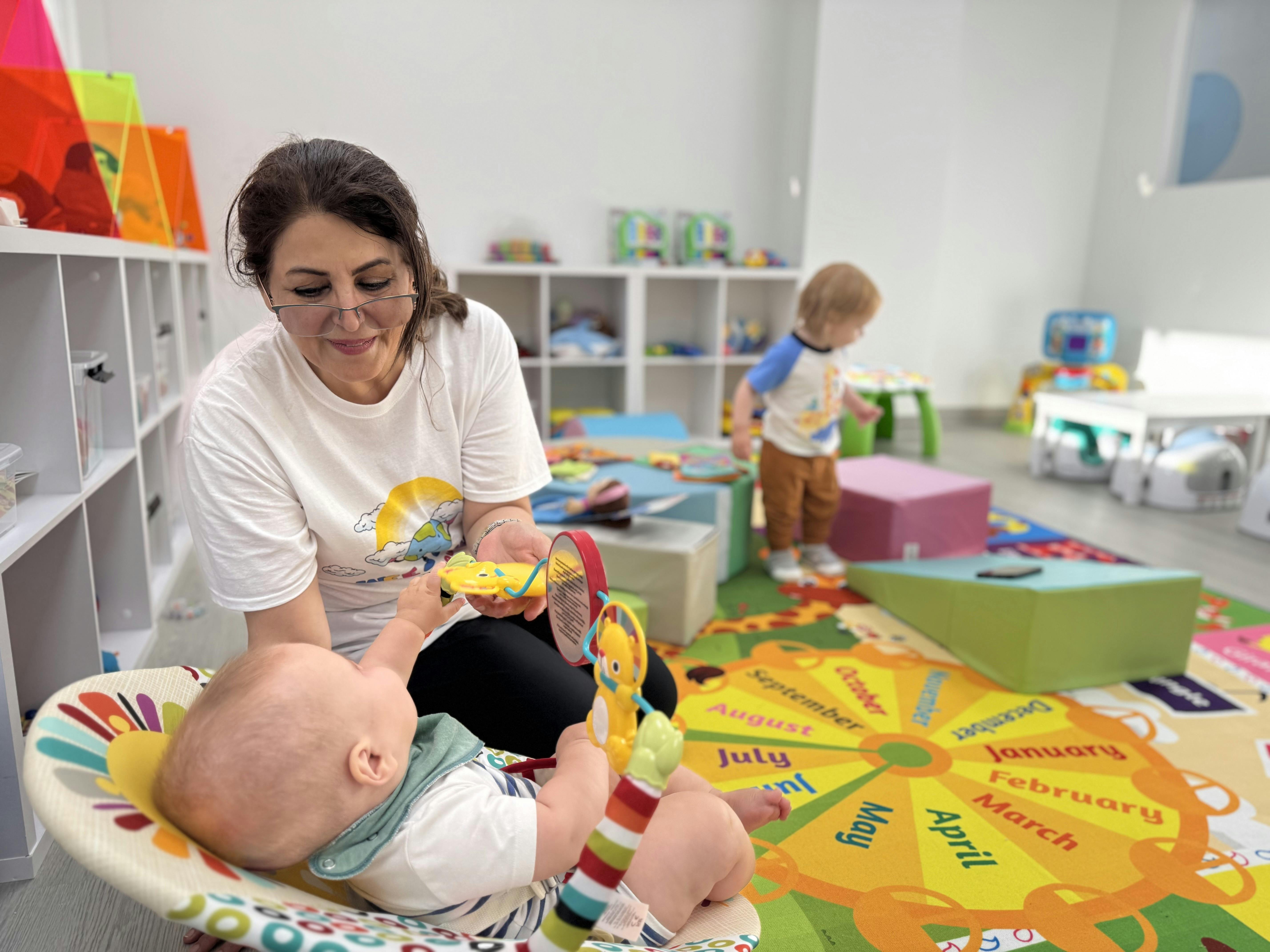 Person interacting with a baby in a bouncer seat in a playroom