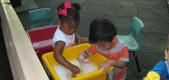 Two children playing with water in a yellow bin