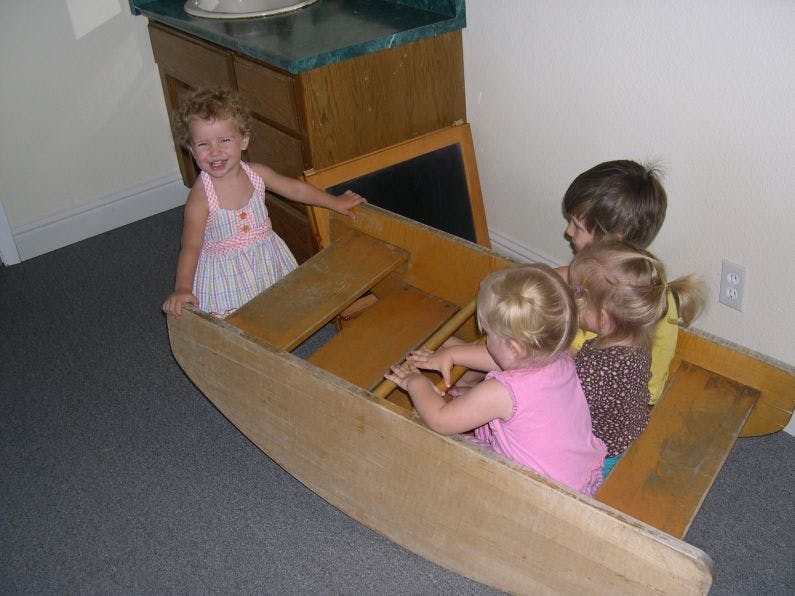 Four children playing in a wooden boat-shaped toy