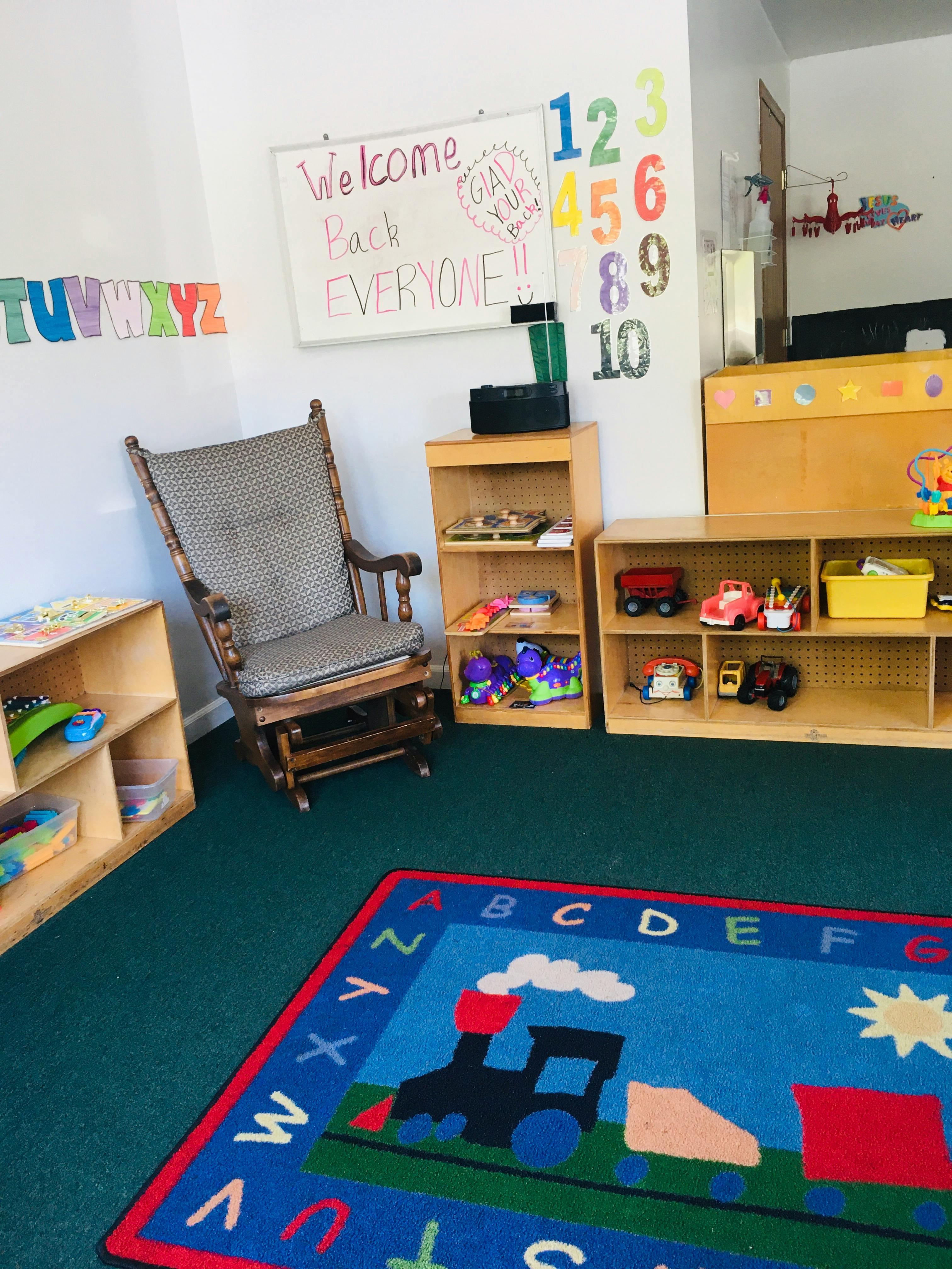 Classroom interior with alphabet rug, rocking chair, and shelves of toys