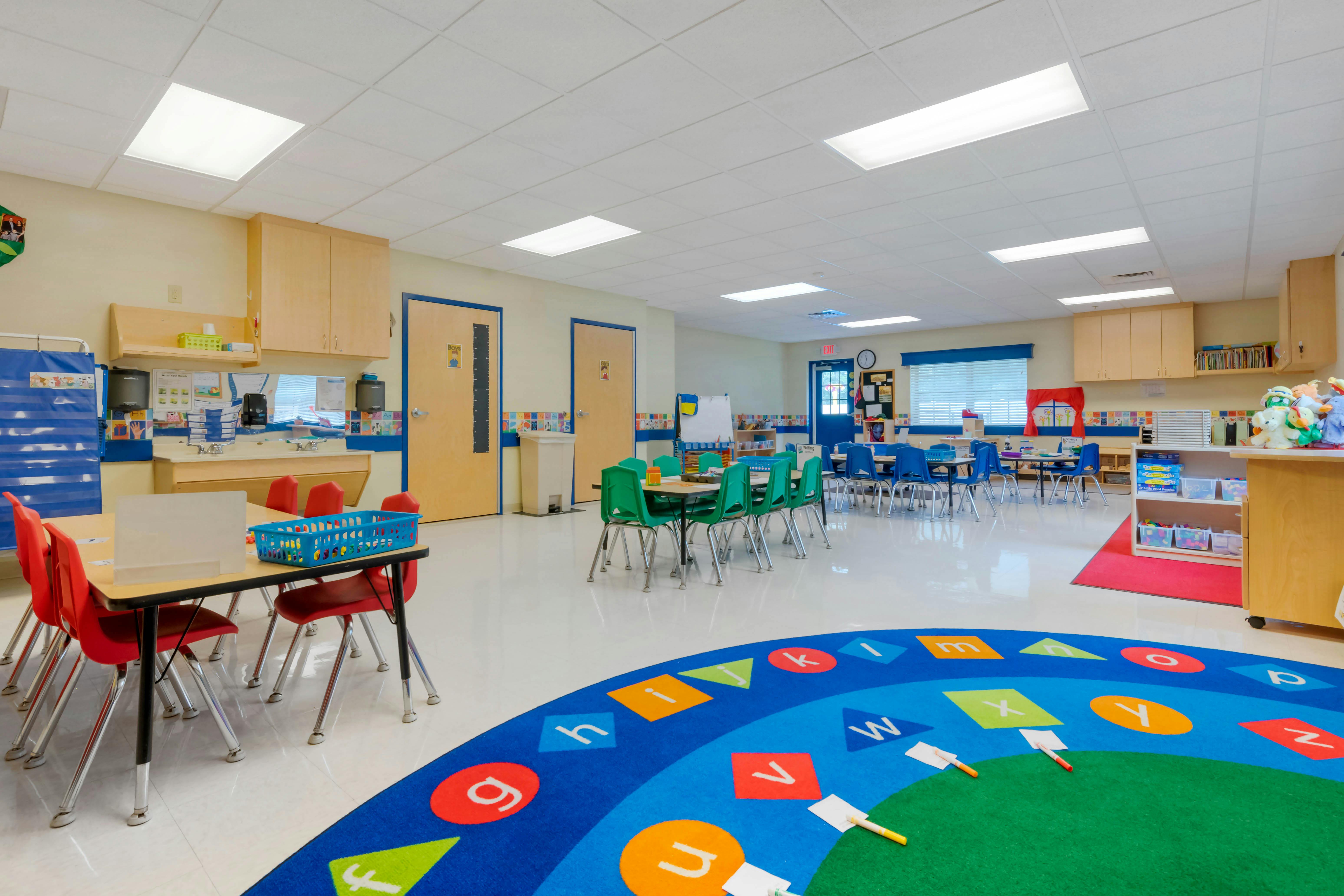 Classroom with tables, chairs, alphabet rug, and wall cabinets
