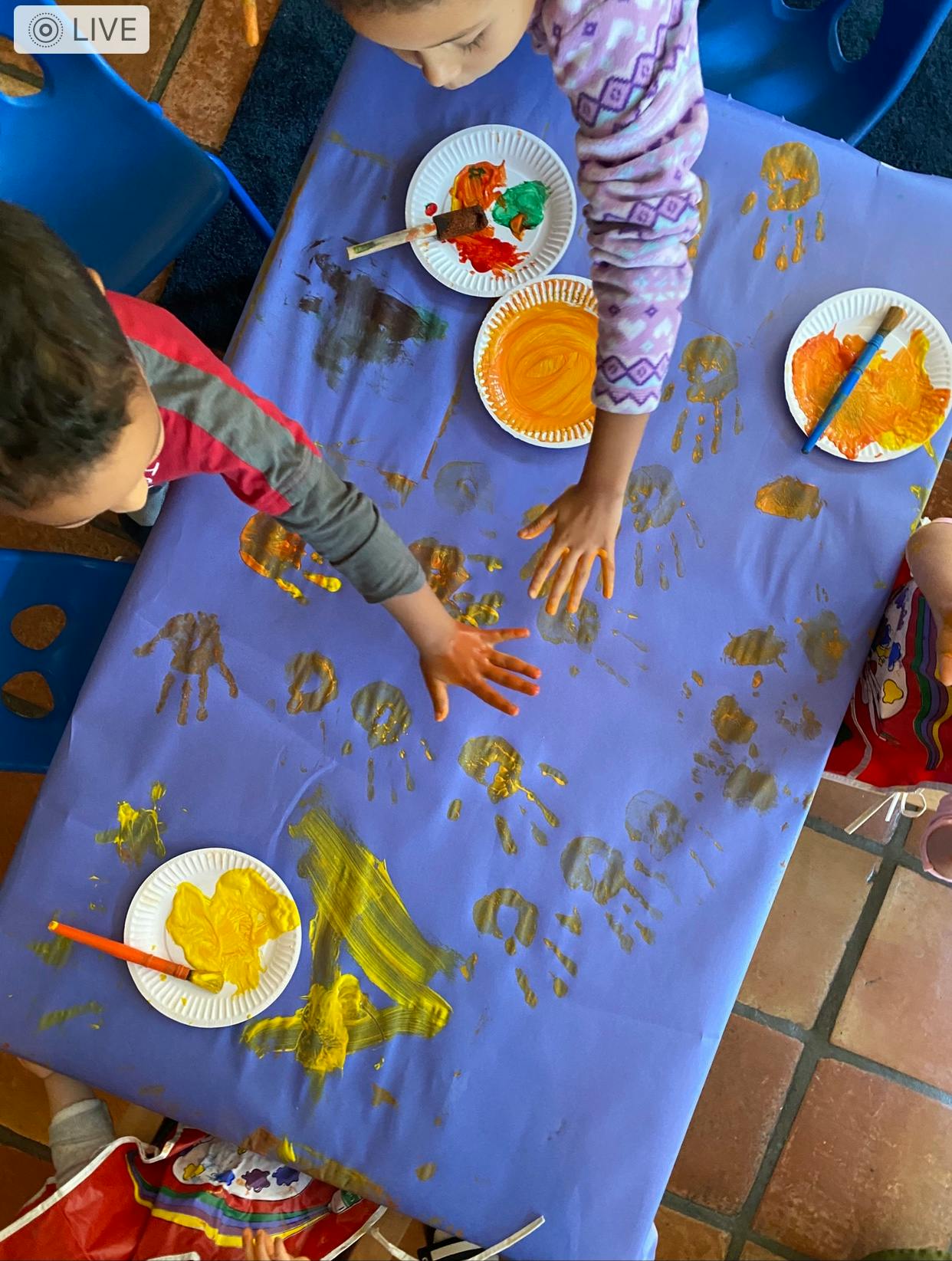 Two children making handprints with paint on a large sheet of paper