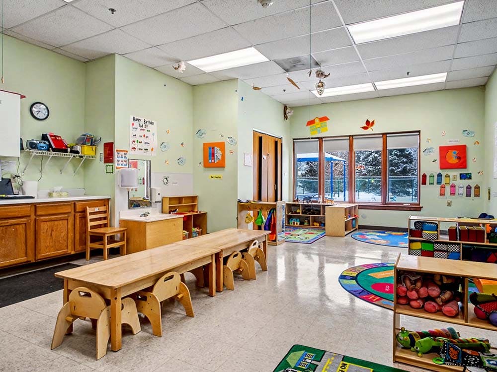 Classroom with small wooden tables and chairs, toys, and window view of snowy trees