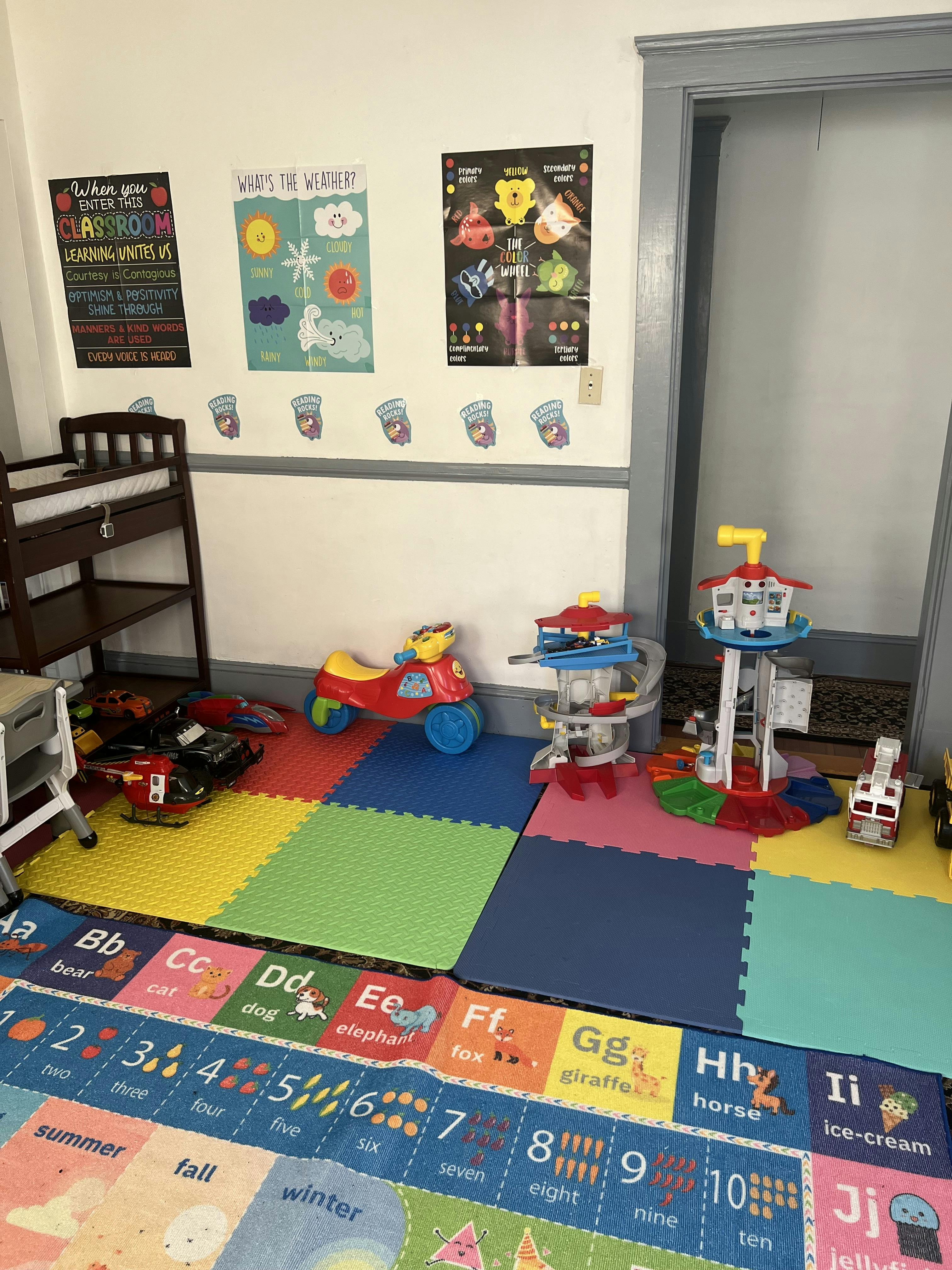 Classroom corner with colorful playmats, toys, and educational posters on the wall