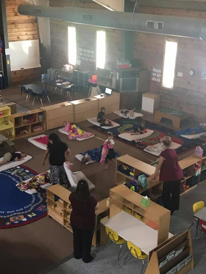 Adults and children in a classroom with children resting on mats