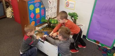 Three children playing at a sand and water table in a classroom