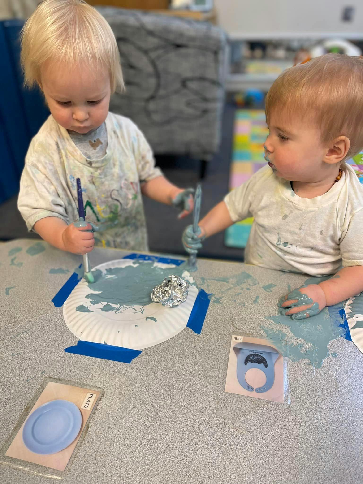 Two children painting paper plates with blue paint