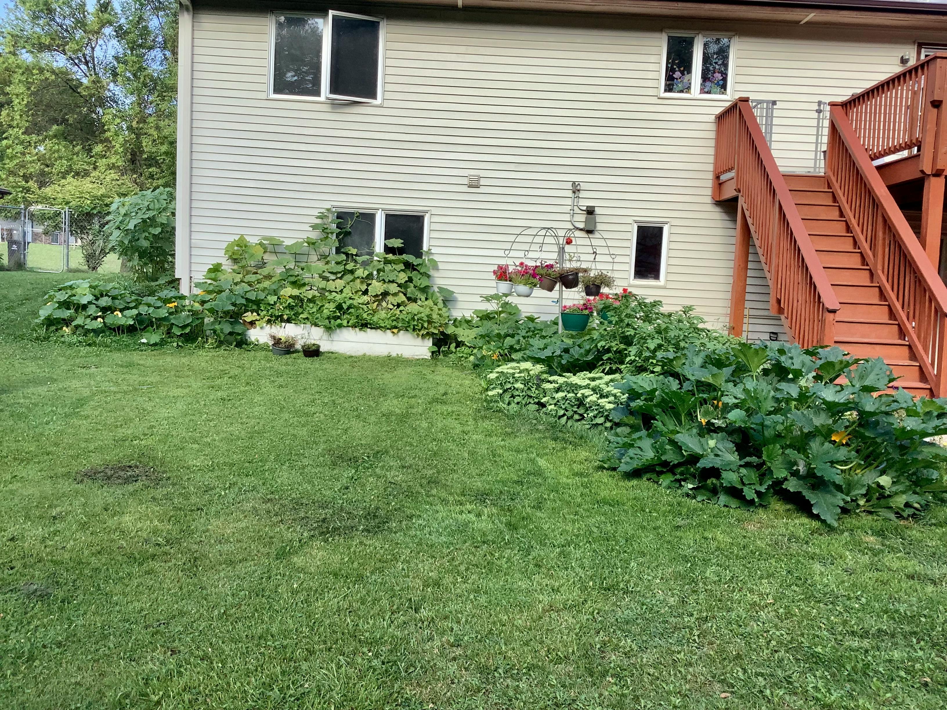House exterior with a wooden deck and stairs, garden beds with plants