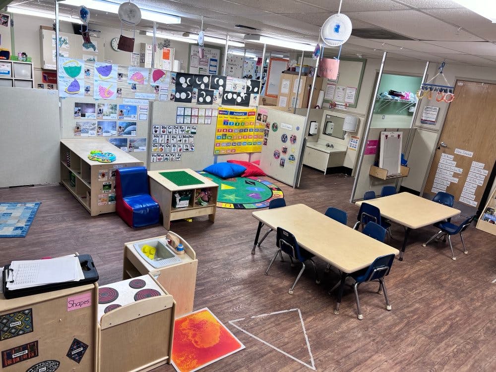 Classroom with child-sized tables and chairs, play kitchen, and educational posters