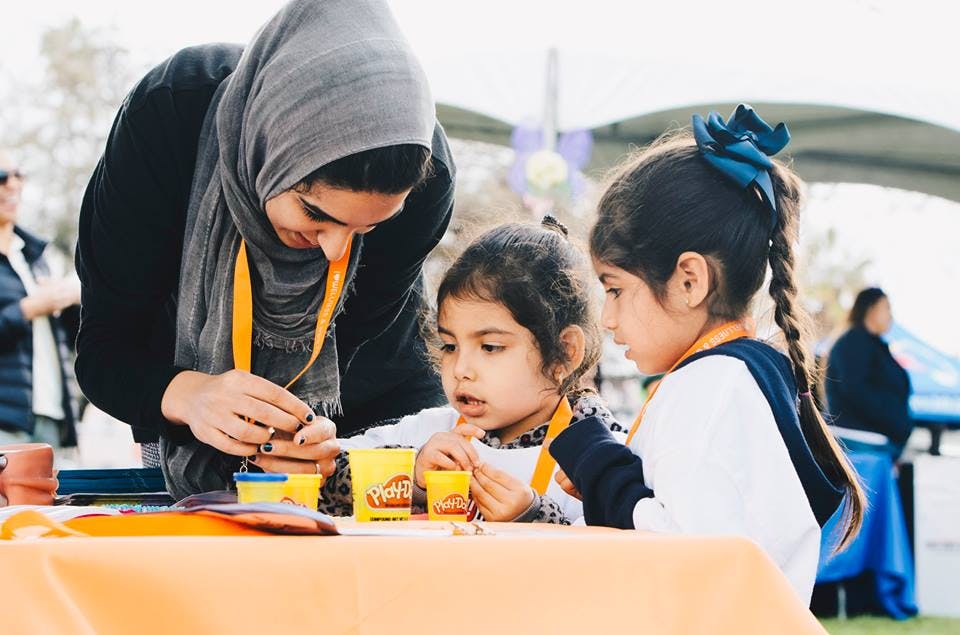 Person in head covering helping two children with playdough