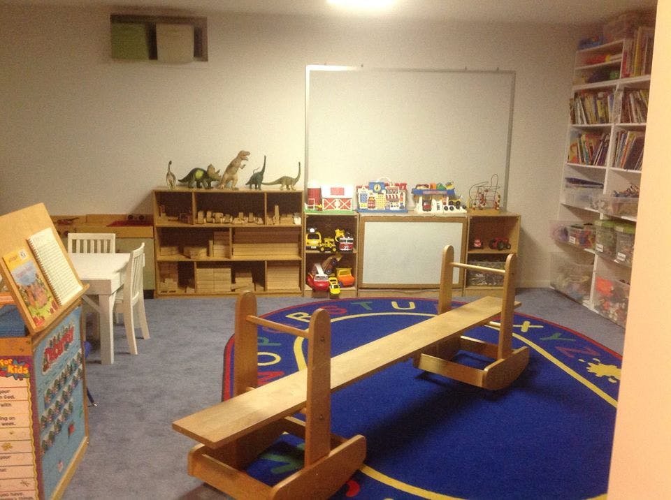 Playroom with wooden seesaw on a blue rug, shelves with toys, and a whiteboard