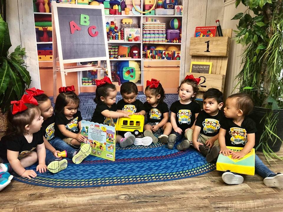 Group of children sitting on a rug playing with toys and a book