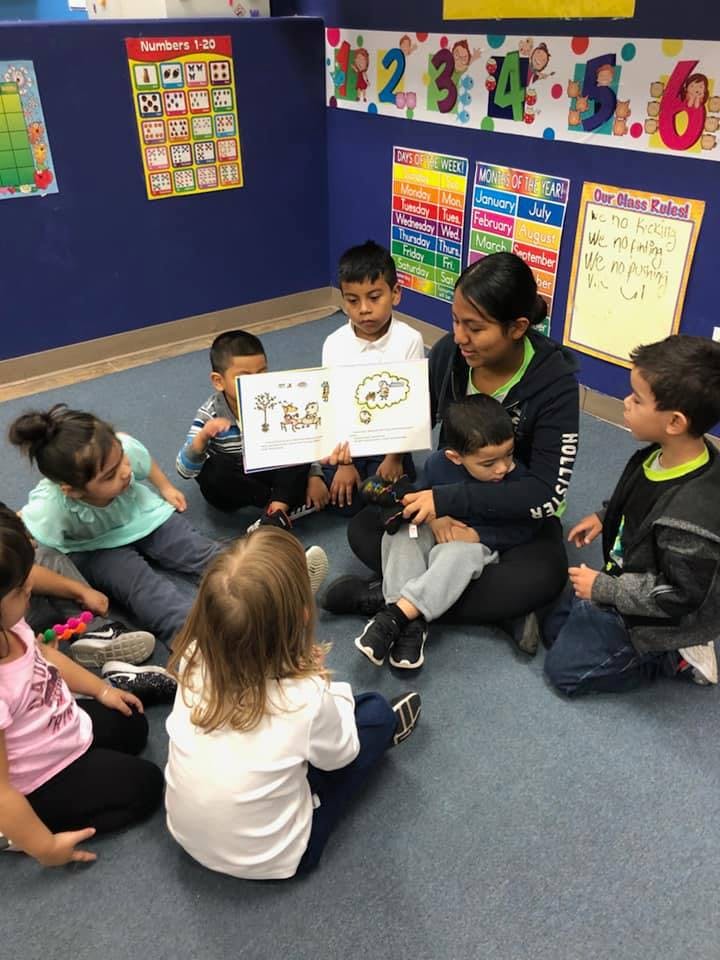 Adult reading a book to a group of children in a classroom