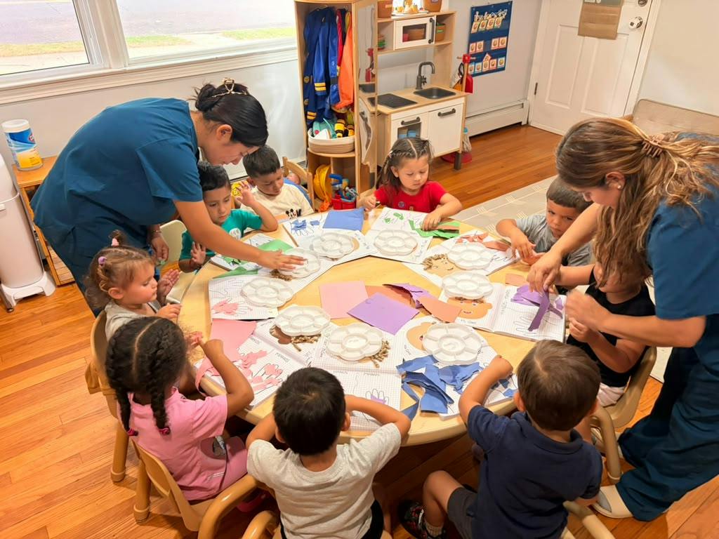 Adults assisting children with a craft project at a circular table in a classroom