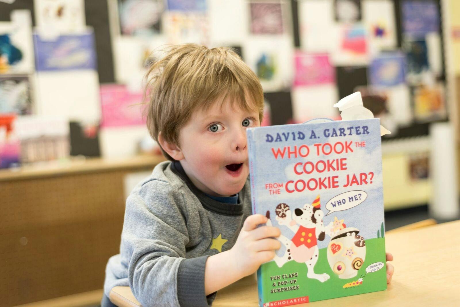 Child holding a book titled "Who Took the Cookie from the Cookie Jar?"