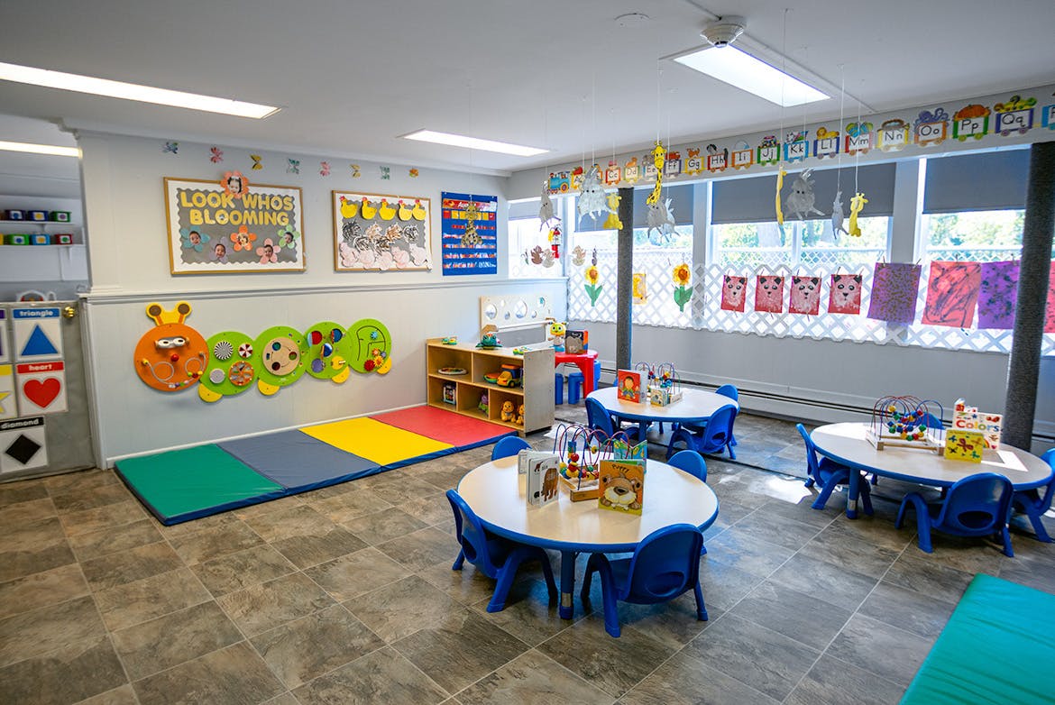 Empty classroom with small tables and chairs, colorful mats on the floor