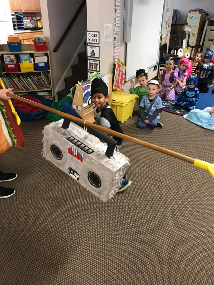 Child in costume holding a stick to hit a boombox-shaped piñata