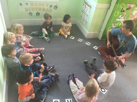 Adult playing guitar for children sitting in a circle on the floor