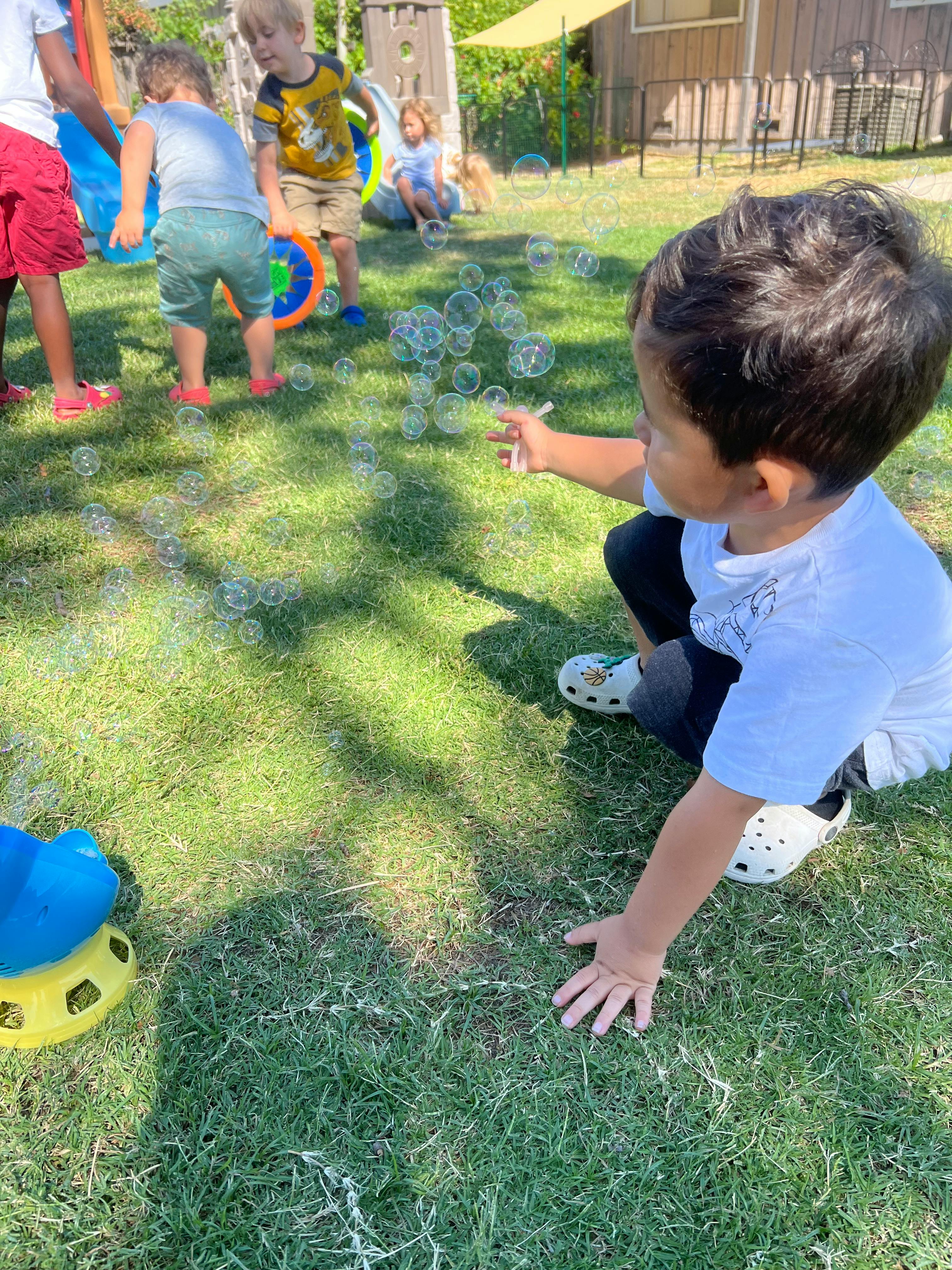 Child reaching for bubbles on grass with other children in background