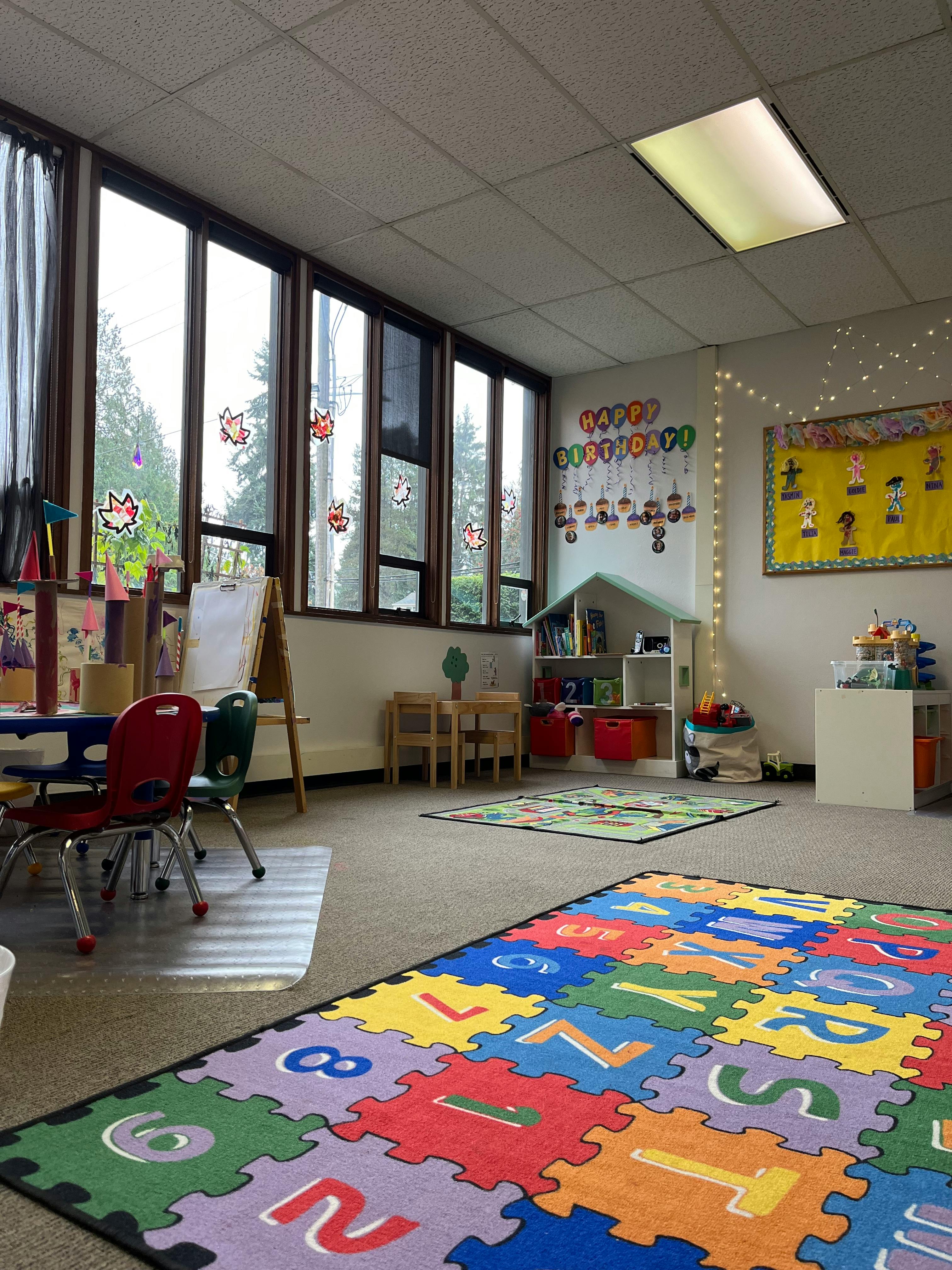 Classroom with large windows, small tables and chairs, and colorful alphabet rug