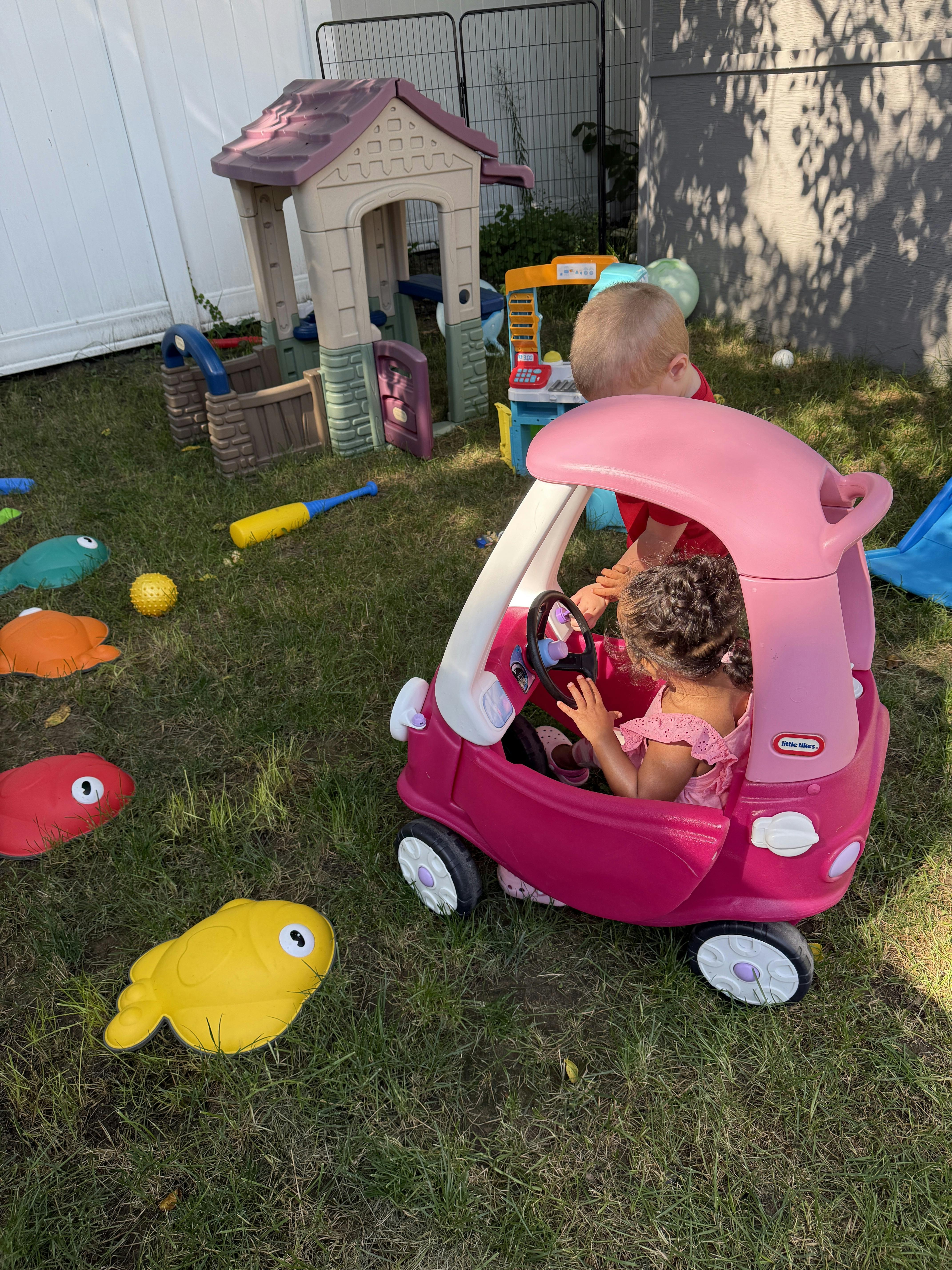 Children playing in a toy car in a backyard