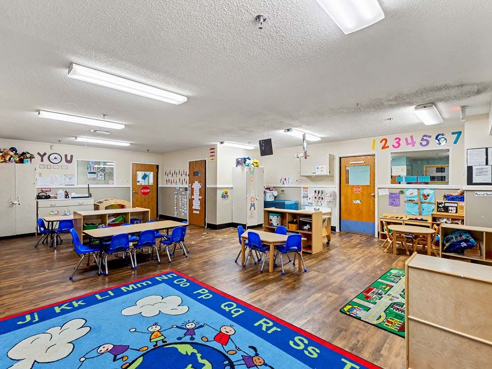 Empty classroom with small tables and chairs, alphabet rug, and numbers on the wall