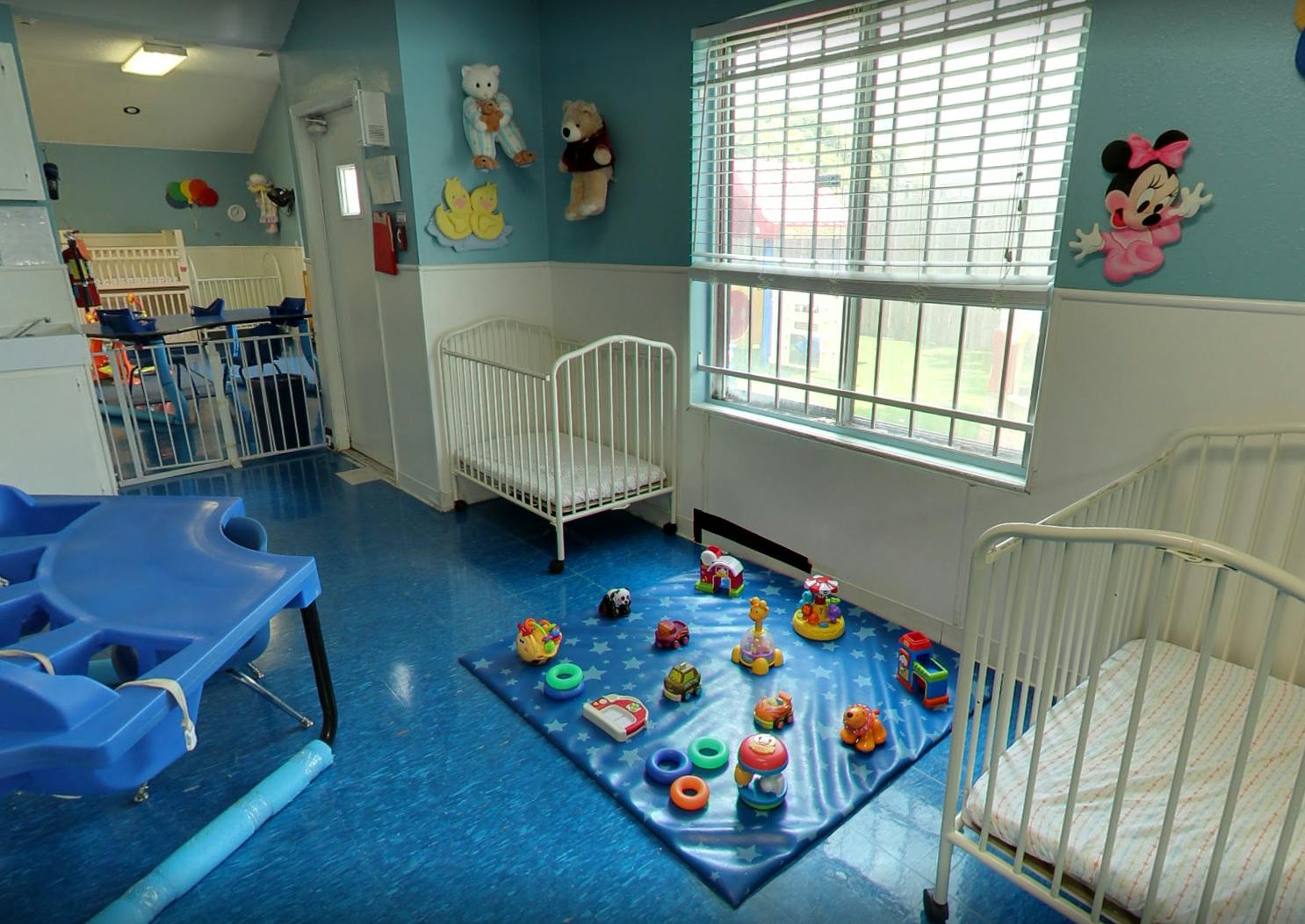 Nursery room with cribs, play mat with toys, and window