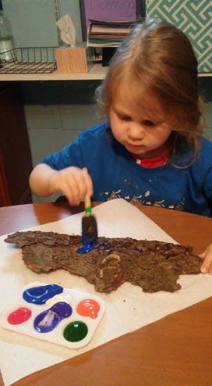 Child painting a piece of bark with a brush