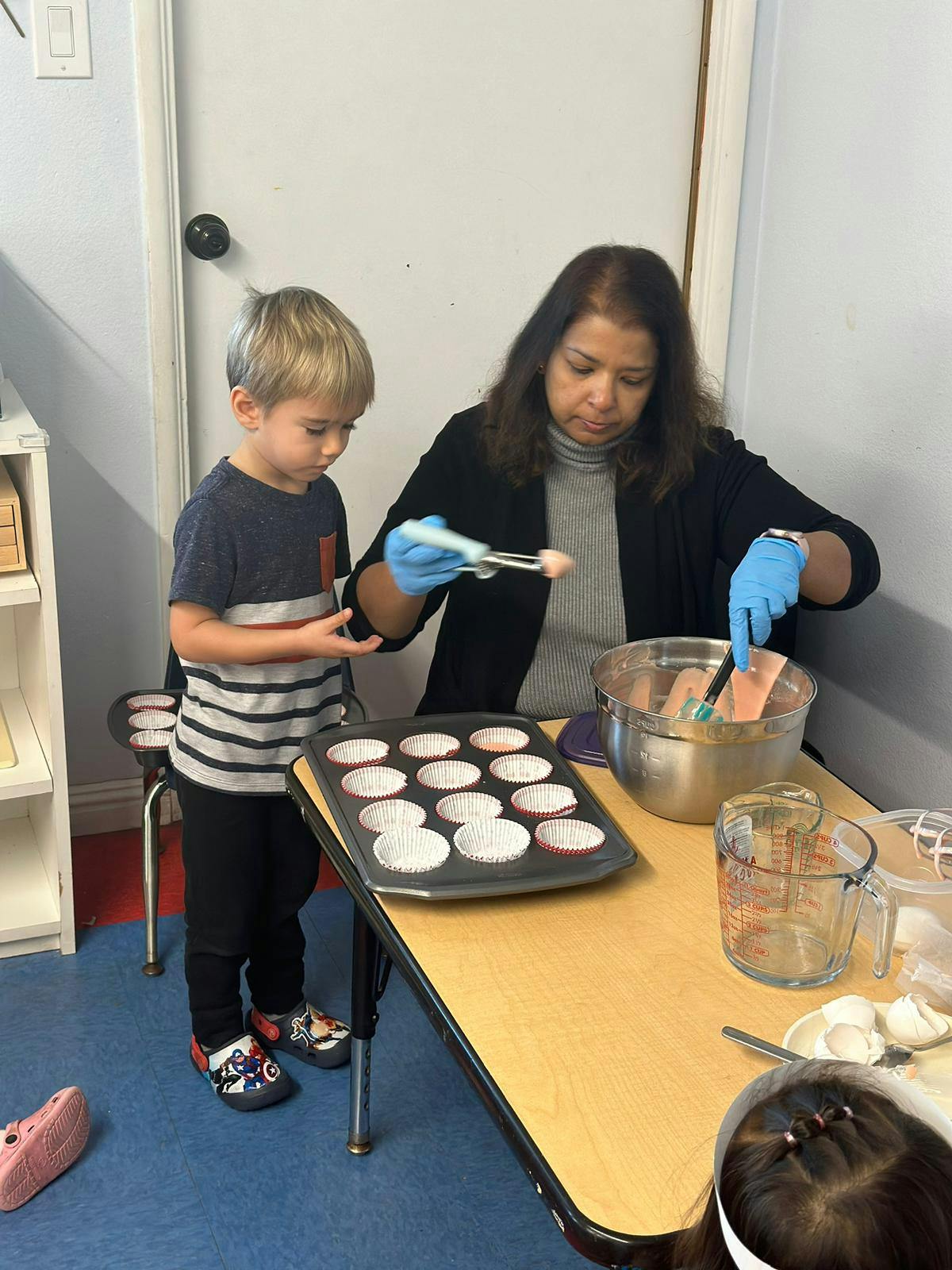 Child and adult preparing muffin batter in a classroom