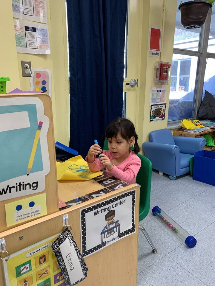 Child sitting at a desk in a classroom holding a marker