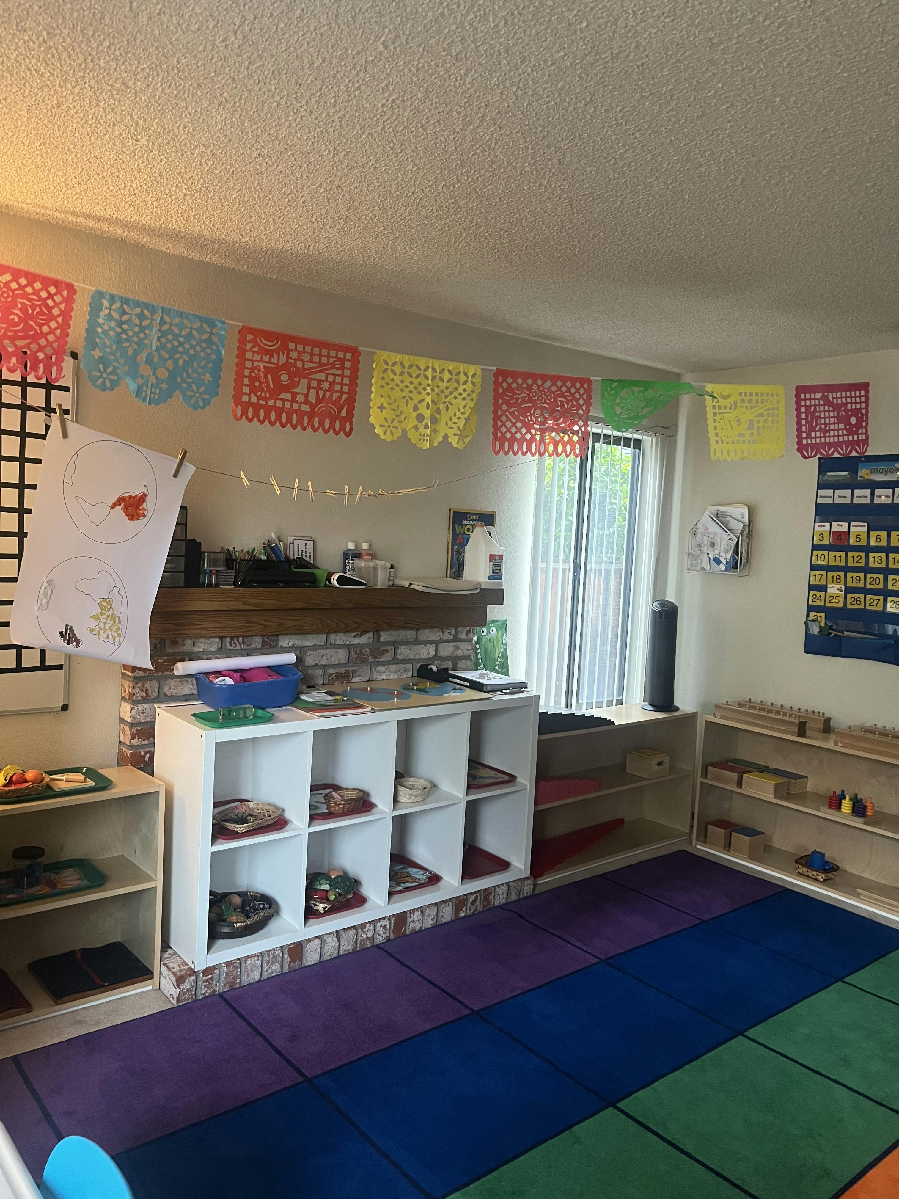Classroom with colorful decorations, shelves with educational materials, and a rainbow rug
