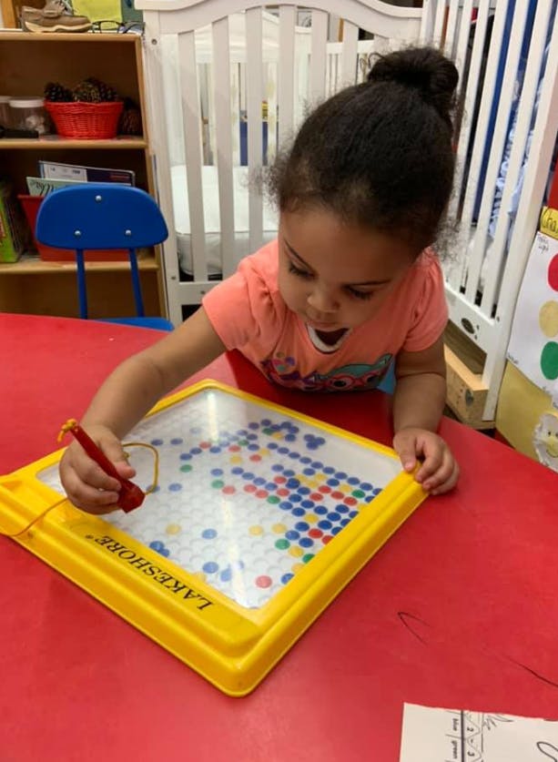 Child playing with a magnetic drawing board on a red table