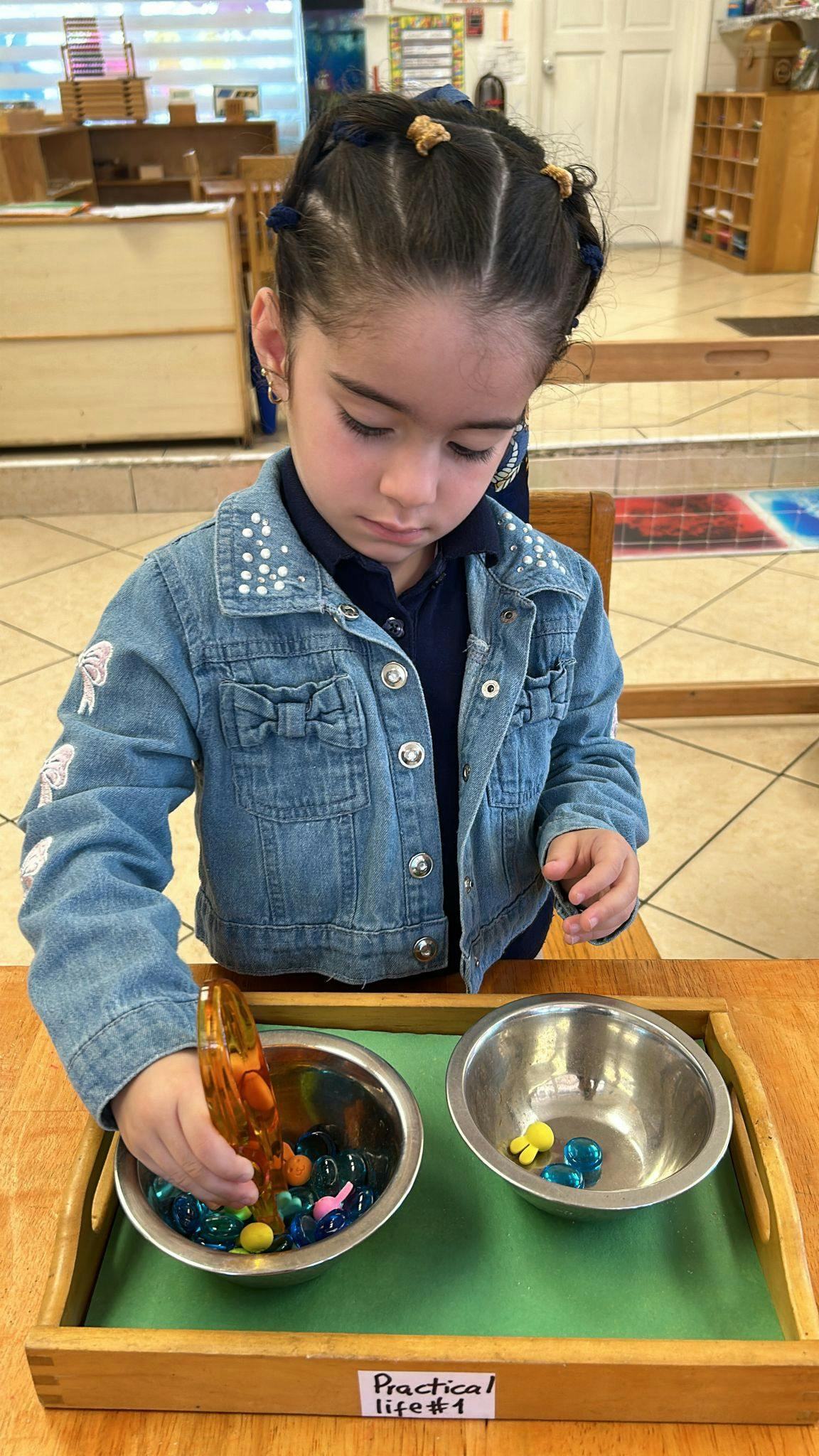Child using tongs to move small objects from one bowl to another