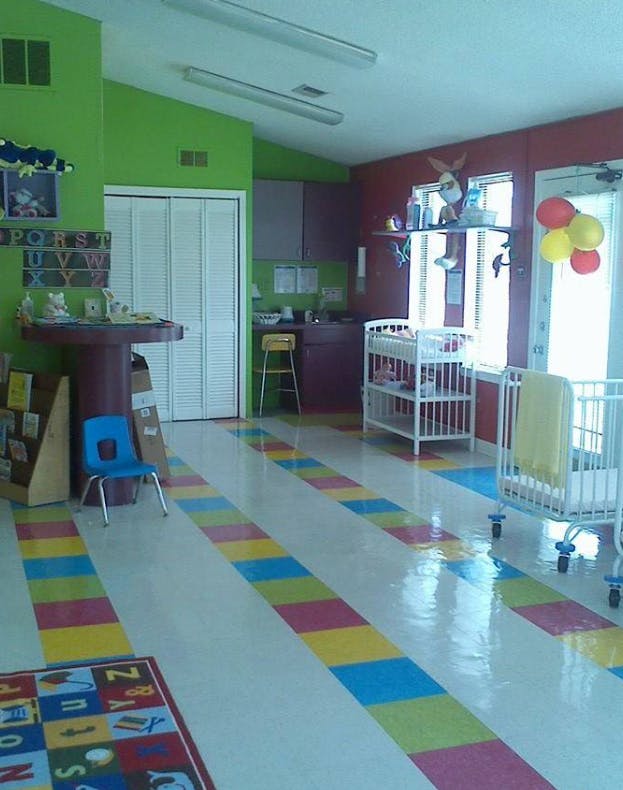 Daycare room with colorful floor, cribs, and small chairs