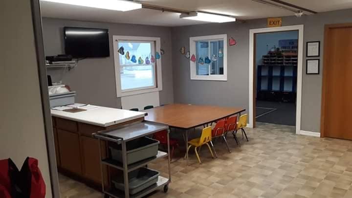 Classroom with a long table and small chairs, counter, and television