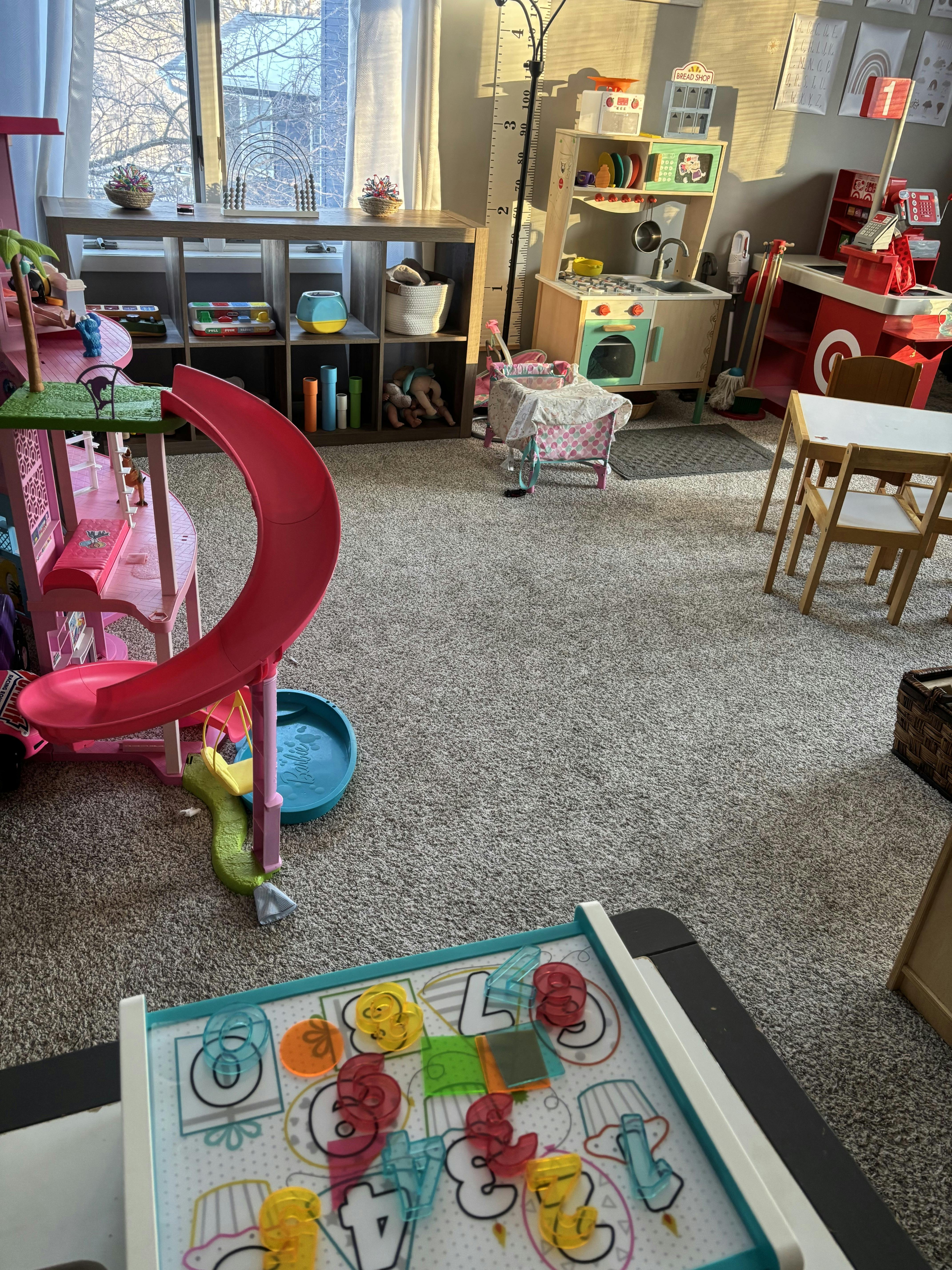 Playroom with toys including a dollhouse with a slide, play kitchen, and small table