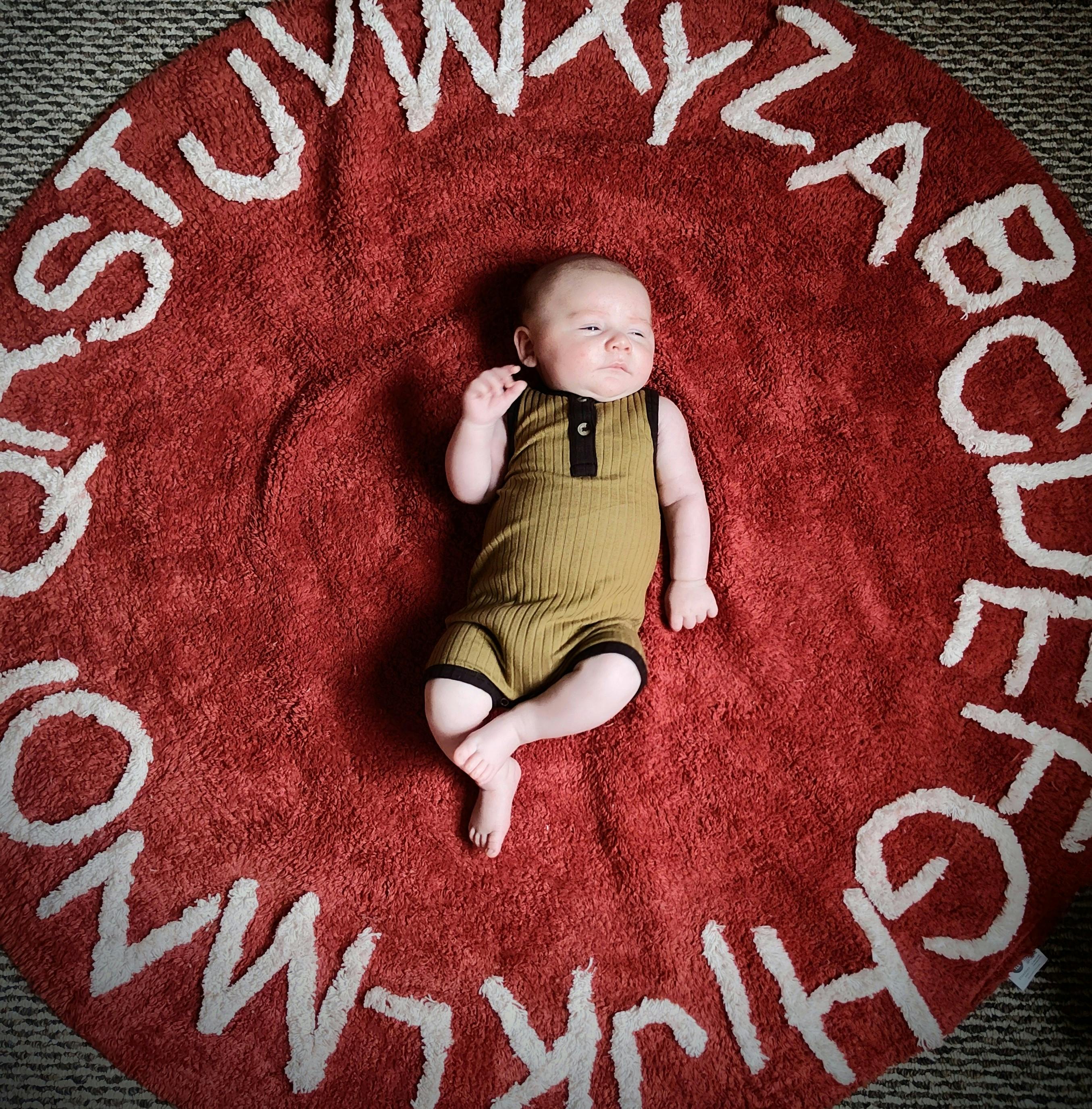 Child lying on a red rug with white alphabet letters
