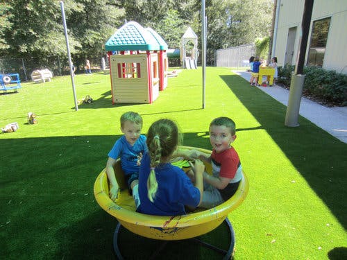 Three children in a yellow spinning toy on a playground