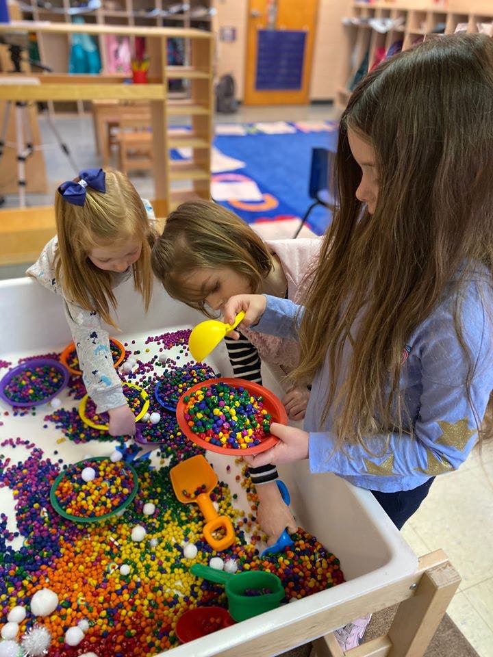 Three children playing with colorful beads and scoops in a sensory bin