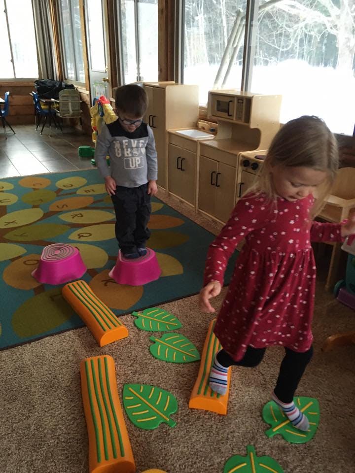 Two children playing with stepping stones and leaf-shaped mats indoors