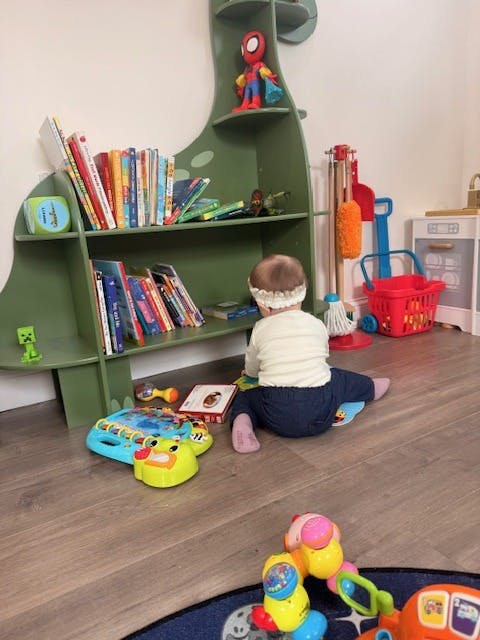 Child sitting on the floor in front of a green dinosaur-shaped bookshelf