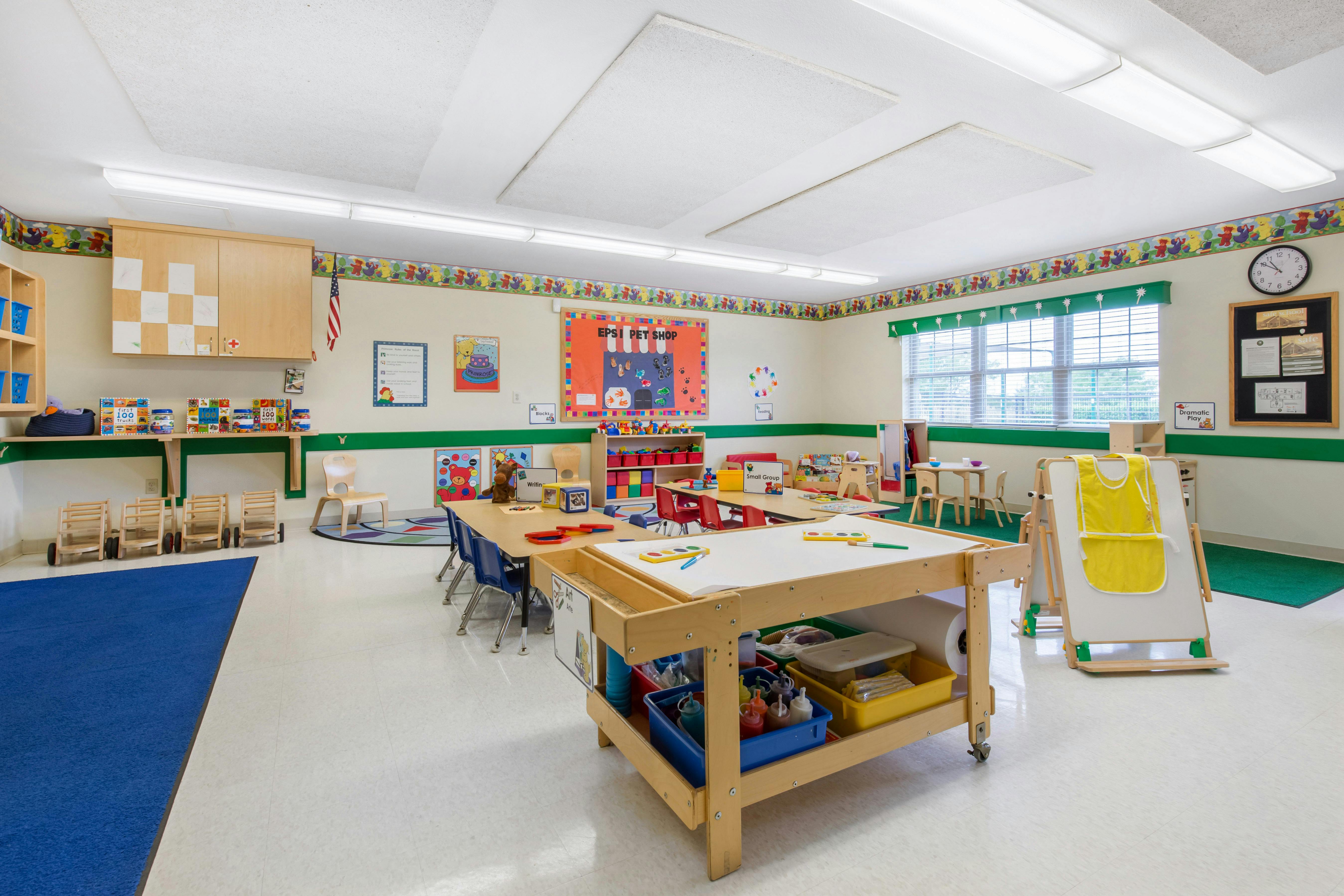 Classroom with tables, chairs, teaching materials, and a blue rug