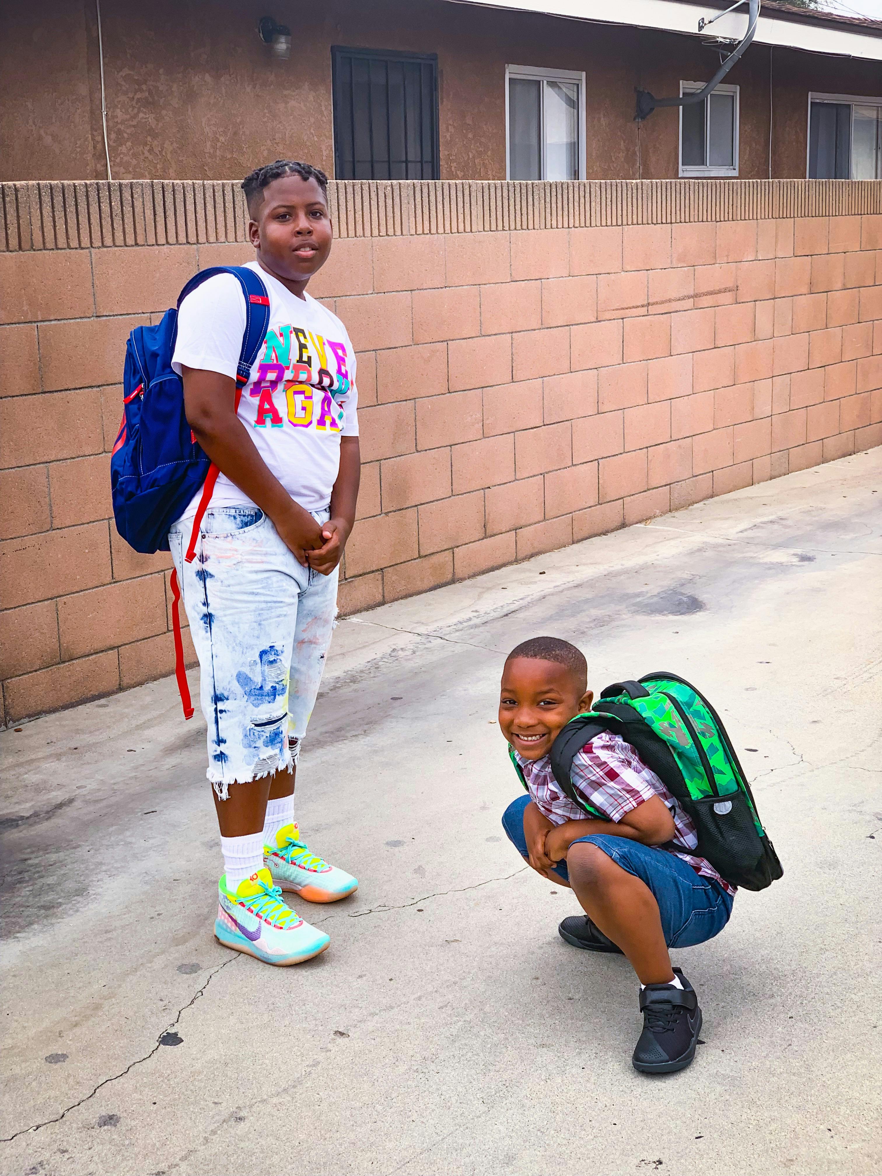 Two children with backpacks, one standing and one crouching