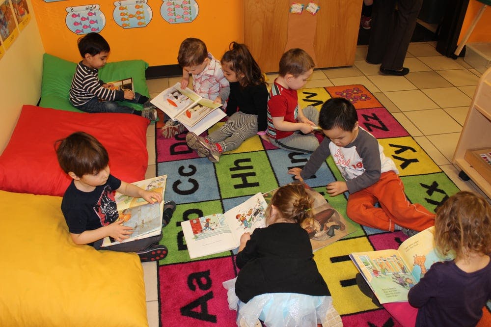 Children sitting on a rug and pillows, reading books
