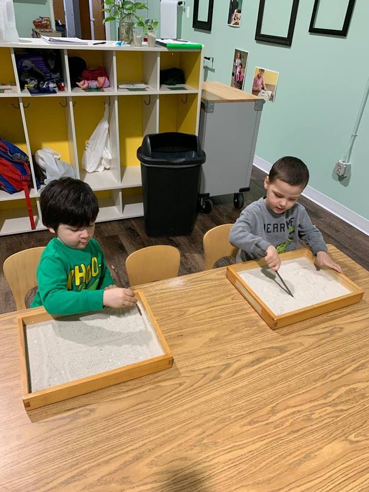 Two children playing with sand trays at a table