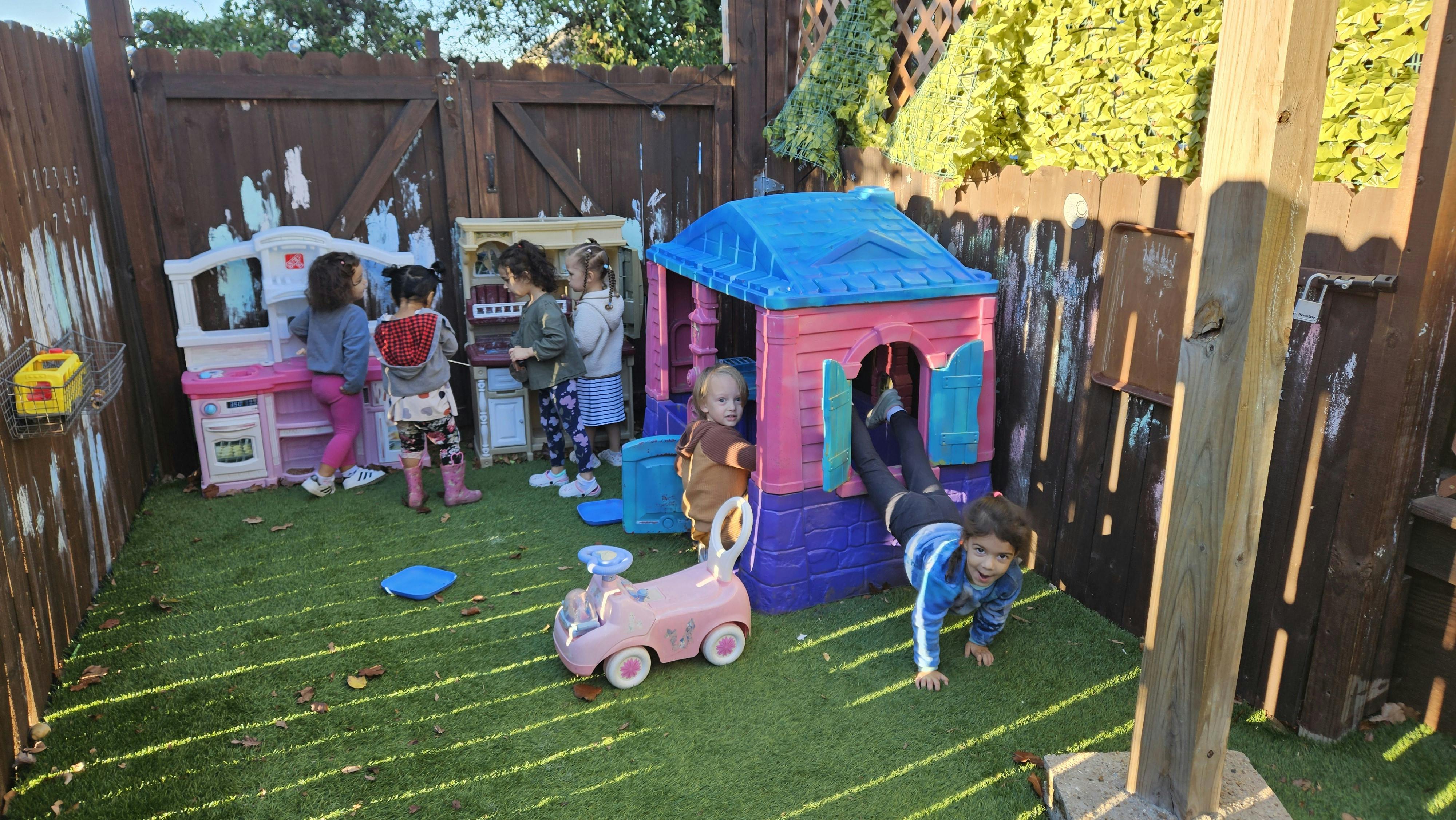 Children playing in an outdoor play area with a playhouse and toy kitchen