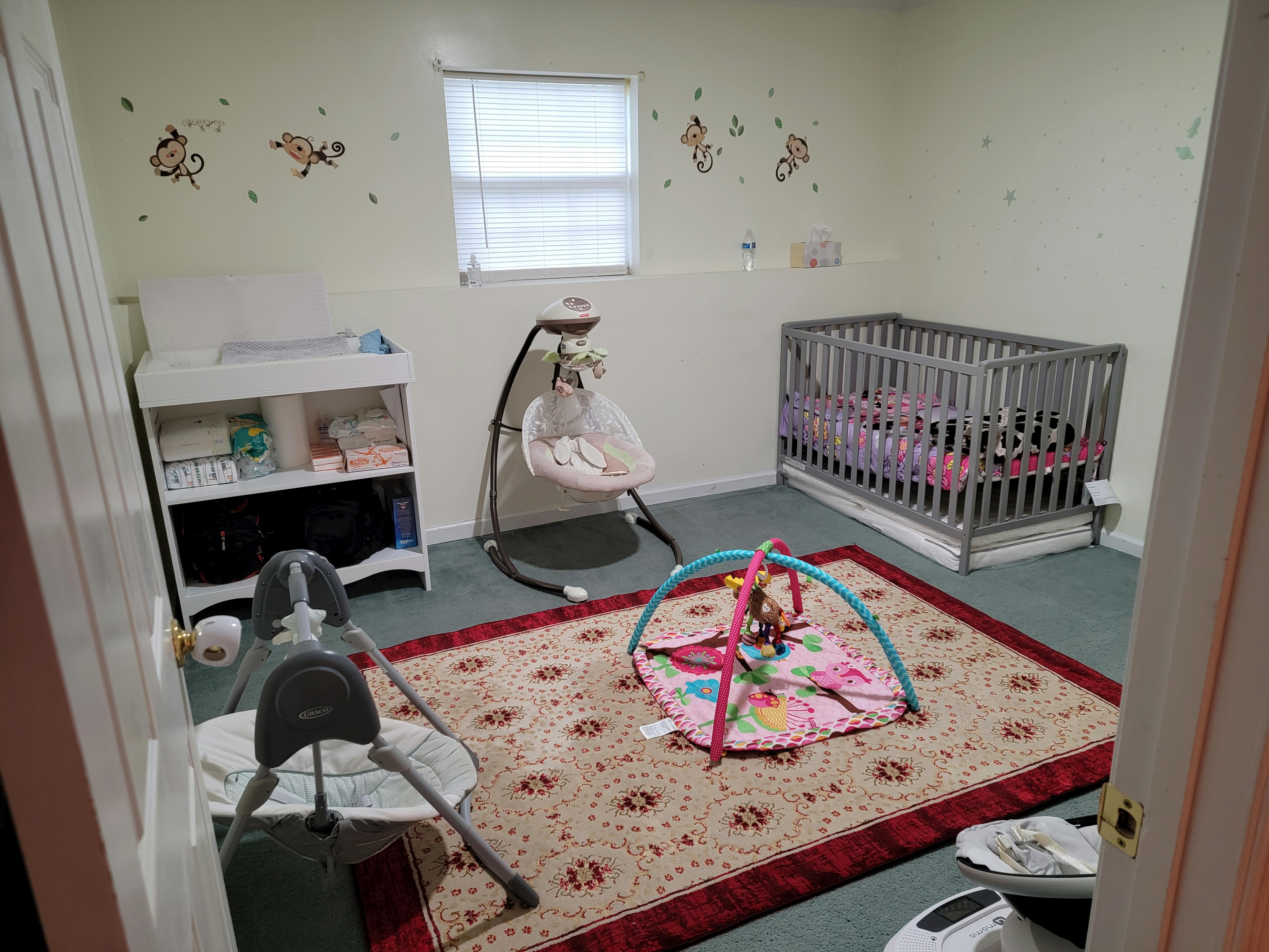 Nursery room with a crib, changing table, baby swing, and play mat